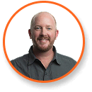 A smiling man with shaved head, beard, wearing dark shirt, in a circle; expert in cannabis lighting technology.