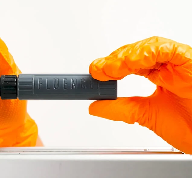 A person in orange gloves holds a FLUENCE LED grow light for cannabis above a table.
