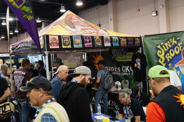 A crowd at a convention gathers around a colorful booth for LED grow lights for cannabis.