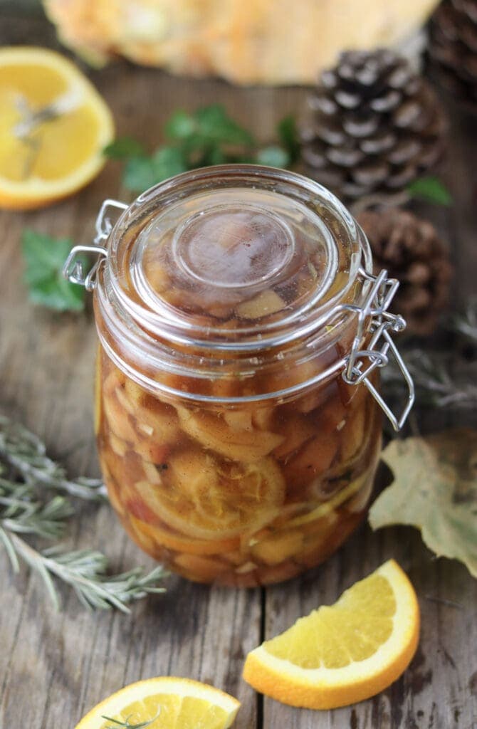 Image of a jar with preserved chicken of the woods (sweet dessert) with oranges and rosemary in the background.