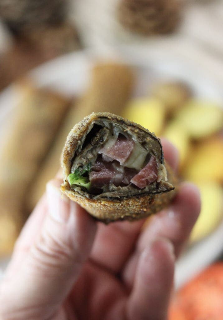 A close shot of sliced fried parasol mushroom roll held in hand, with melted mozzarella, bacon and fresh young onion slices inside the roll.