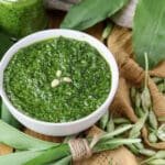 Pesto with wild garlic and toasted pine nuts served in a bowl with wild garlic leaves in the bacground.