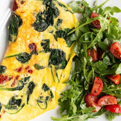 A sun-dried tomato omelette stuffed with spinach and fresh mozzarella, with a green arugula and tomato salad on the side.