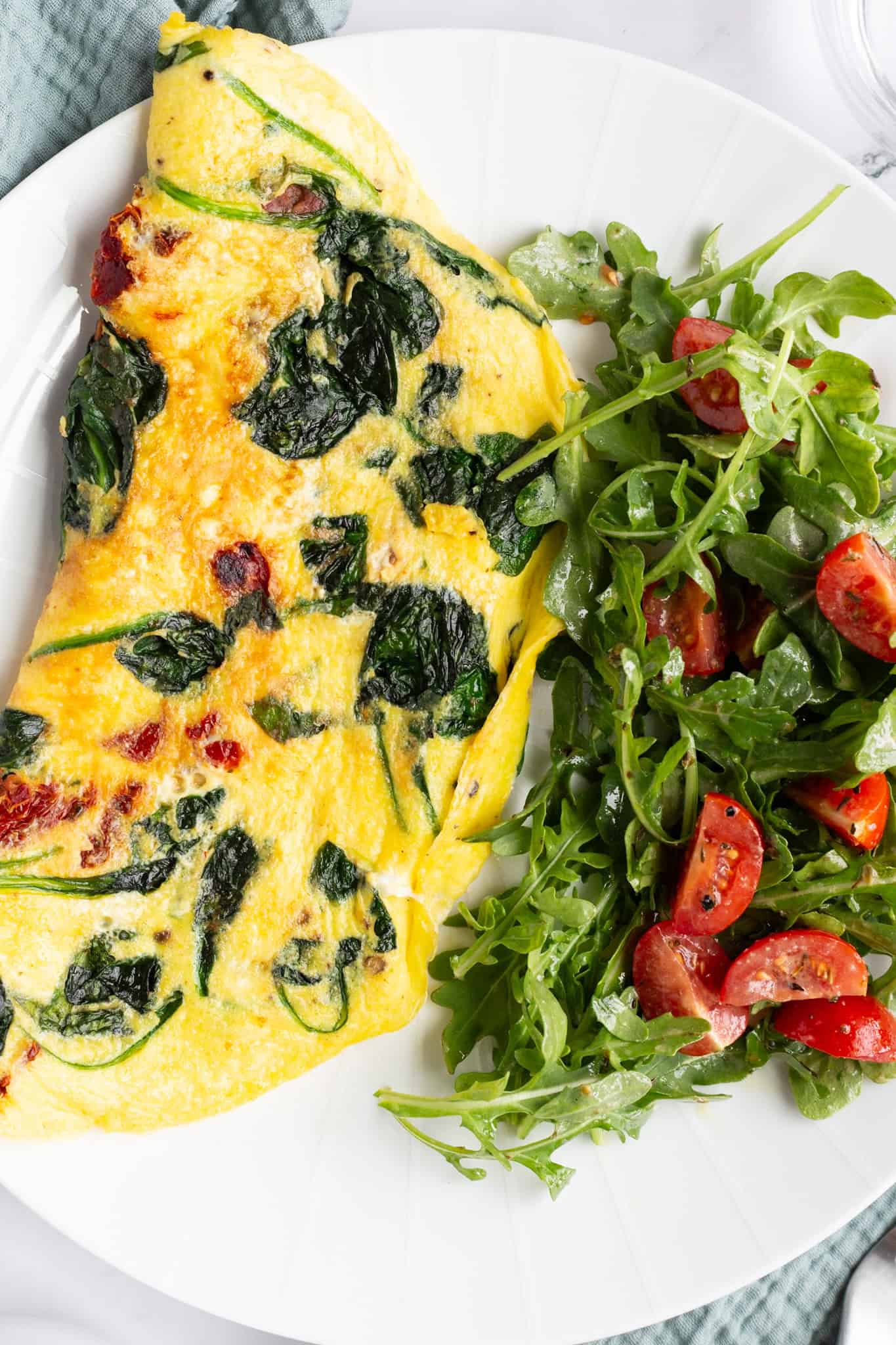 A sun-dried tomato omelette stuffed with spinach and fresh mozzarella, with a green arugula and tomato salad on the side.