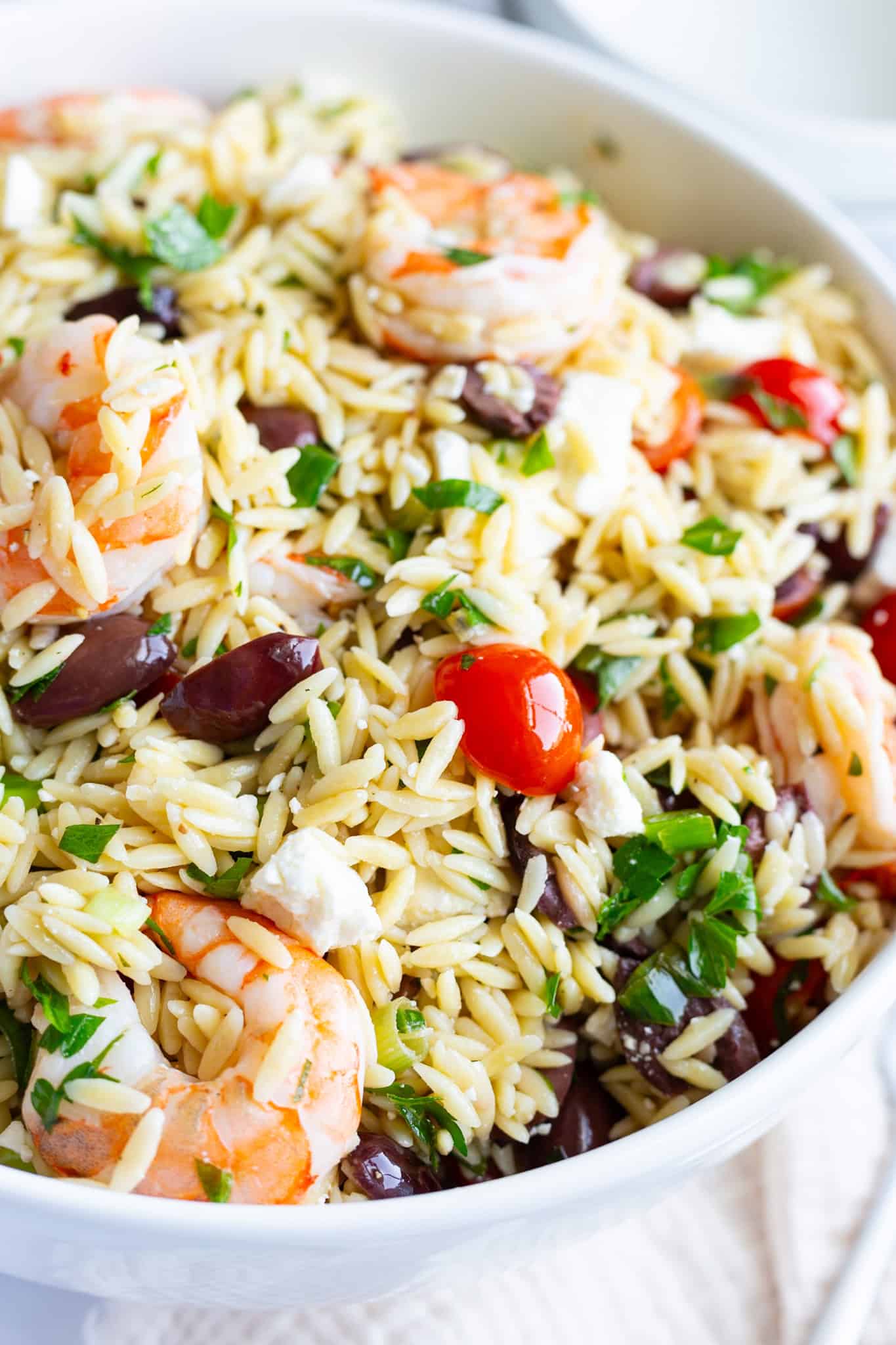 A large bowl of Mediterranean shrimp orzo salad with olives, cherry tomatoes, and fresh herbs.