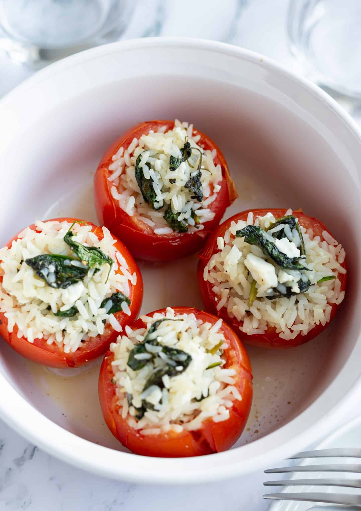 Four stuffed tomatoes with rice topped with spinach and feta.