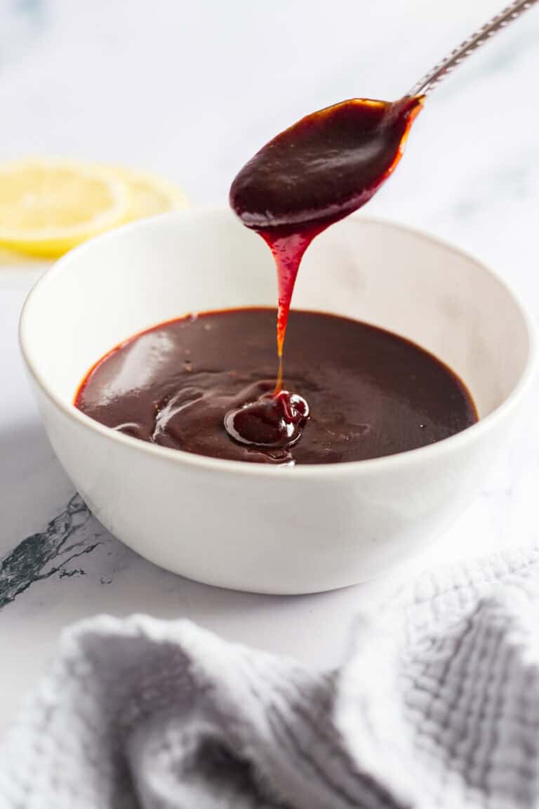 A spoon drizzling barbecue sauce into a bowl filled with the sauce.