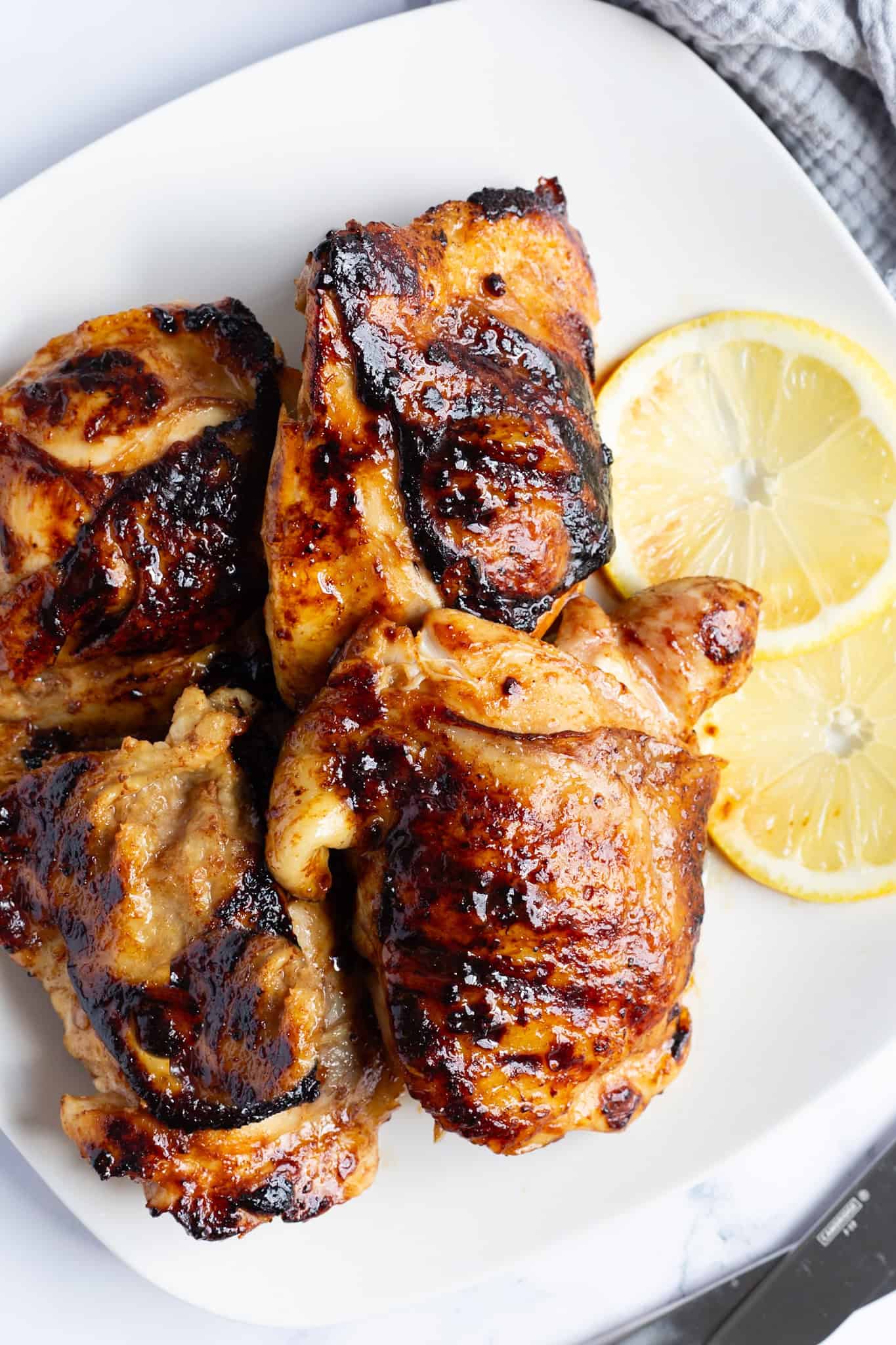 A platter of grill pan chicken thighs with sliced lemon on the side.