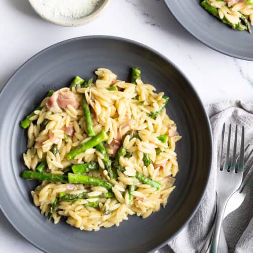 A grey plate of orzo with asparagus and Parmesan with bits of torn prosciutto.