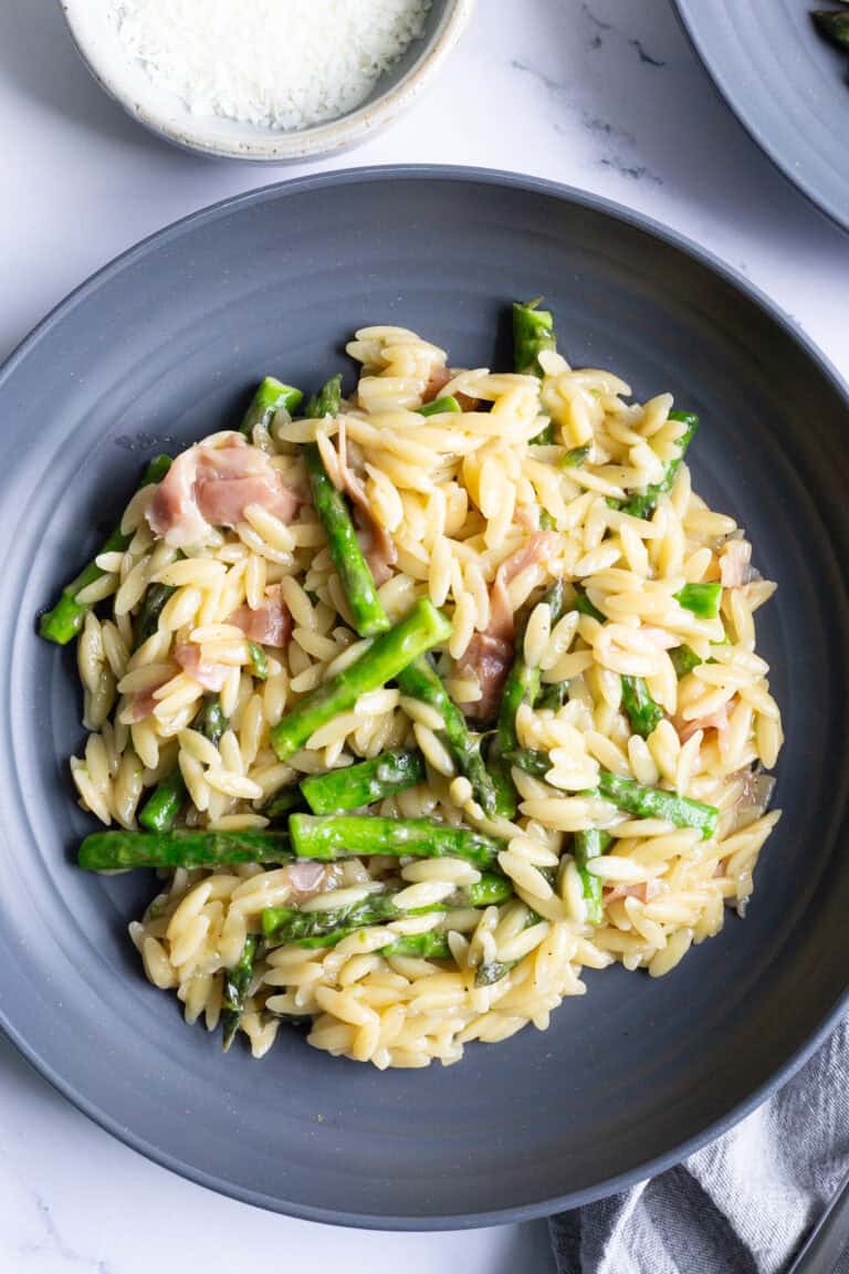 A grey plate of orzo with asparagus and prosciutto.