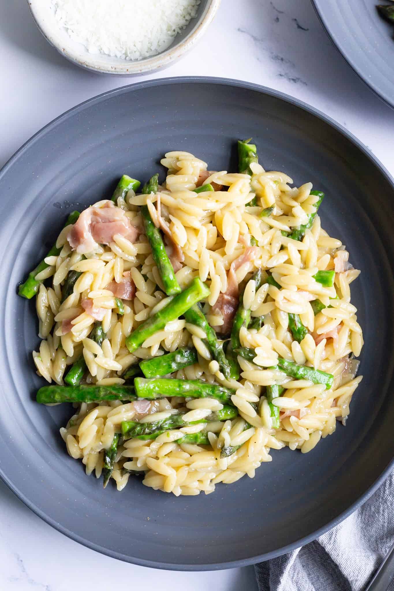 A grey plate of orzo with asparagus and prosciutto.