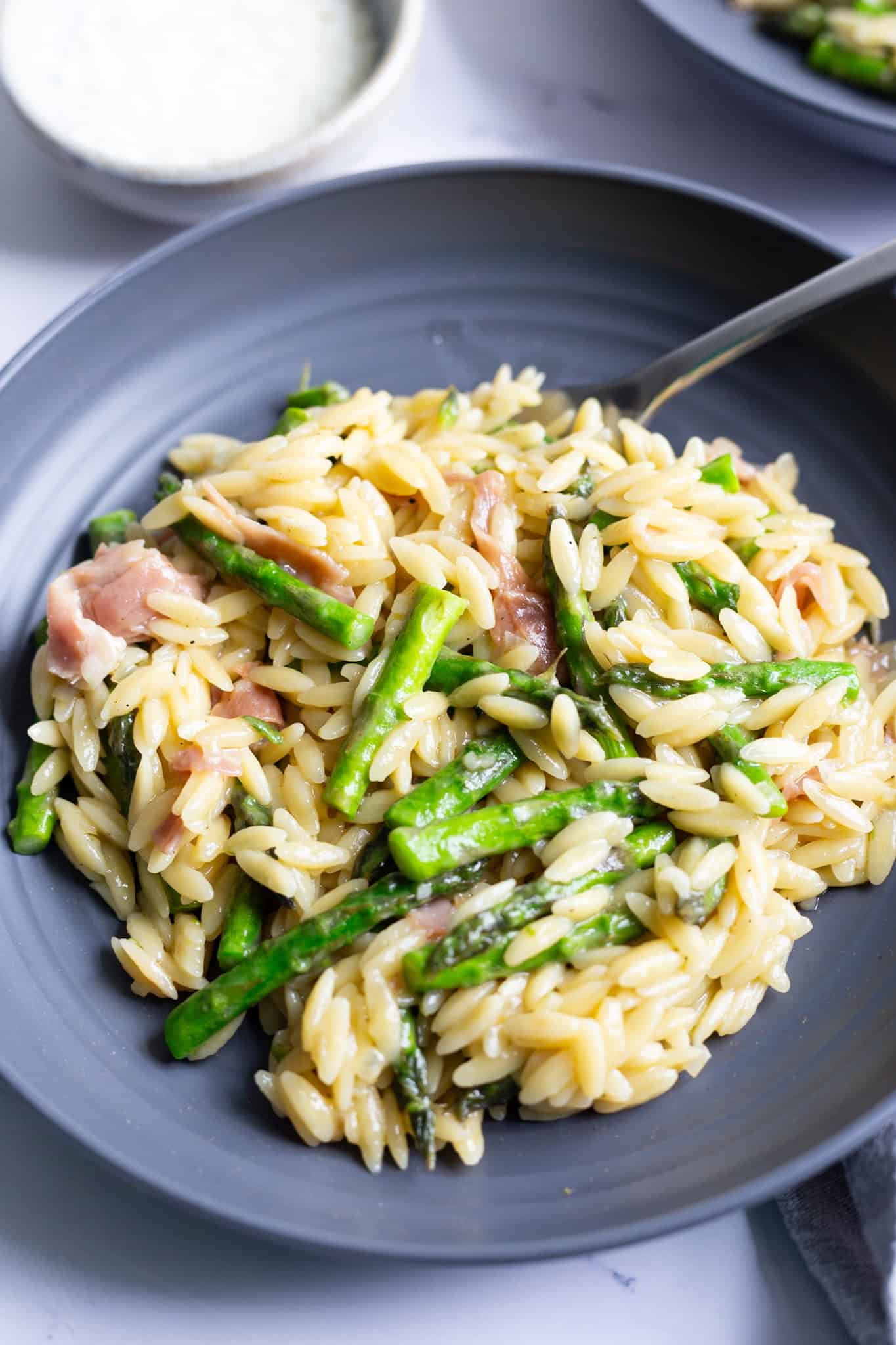 A plate of creamy orzo with asparagus, prosciutto, and Parmesan.