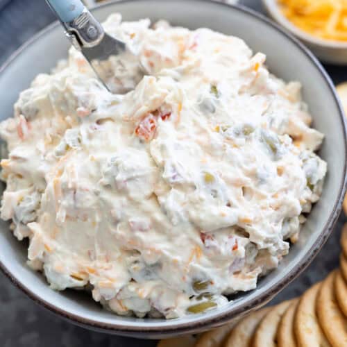 A bowl of olive dip with almonds on a platter filled with crackers.