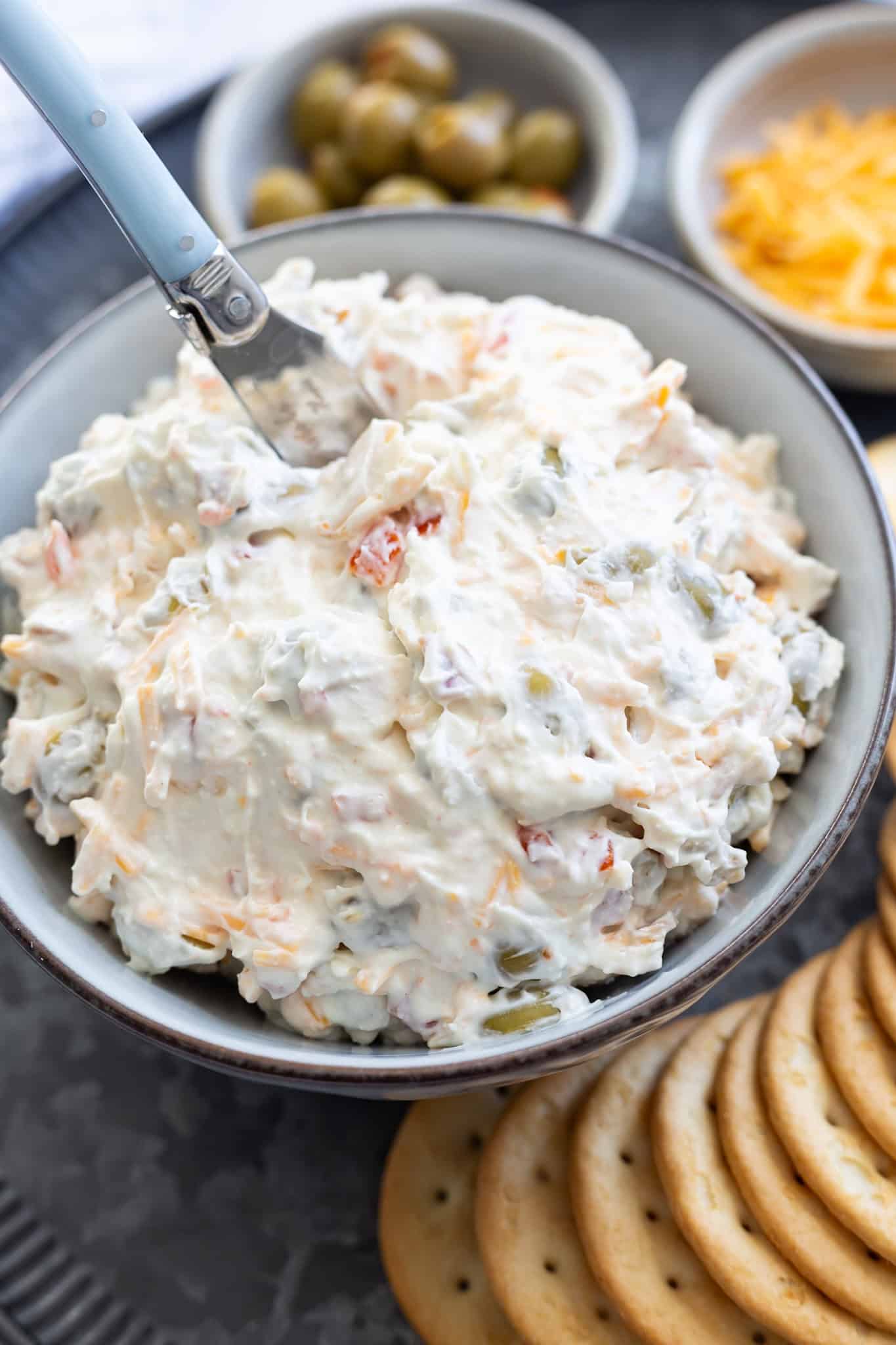 A bowl of olive dip with almonds on a platter filled with crackers.