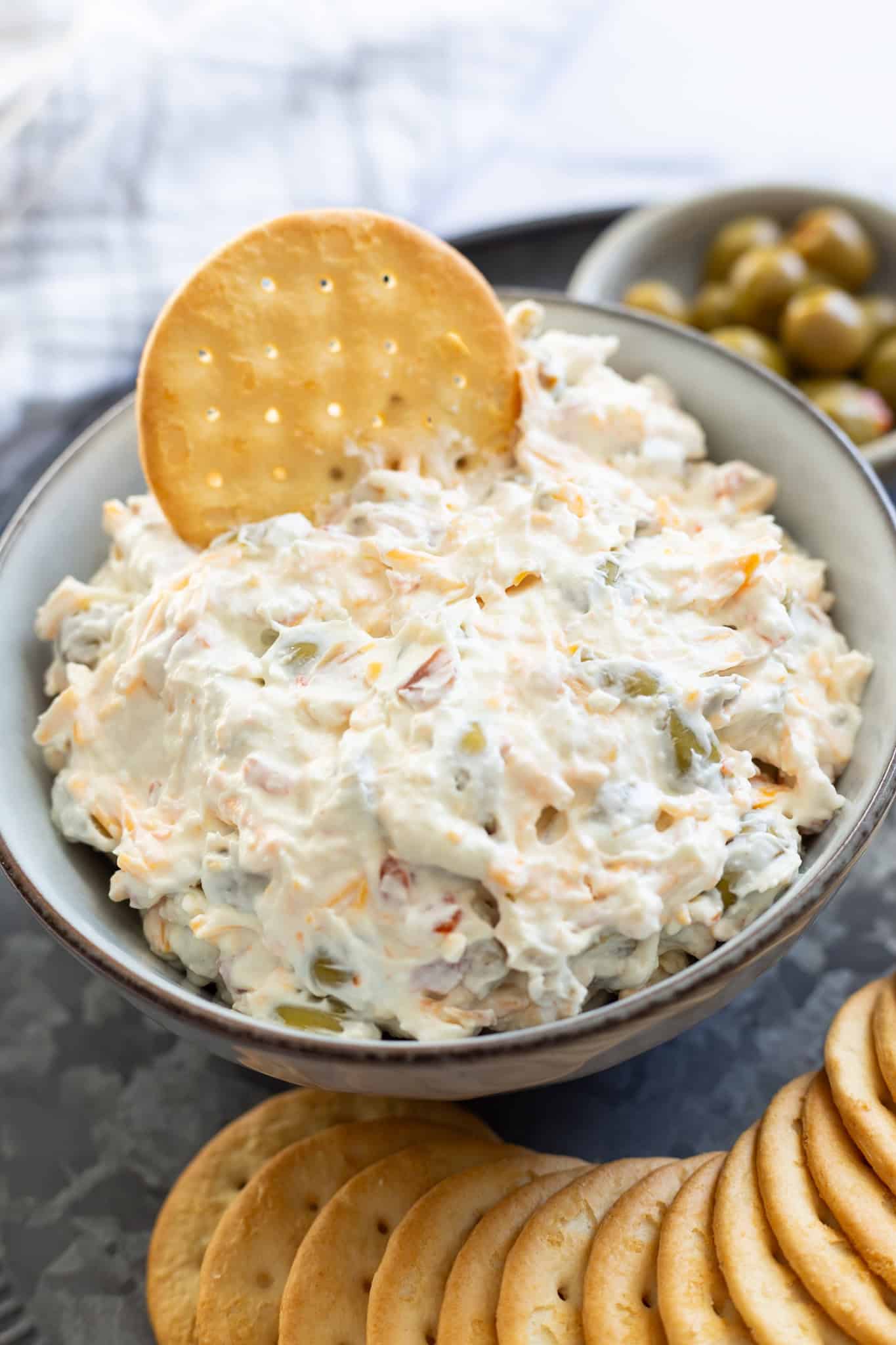 A bowl of olive dip with a buttery cracker sticking out of it.