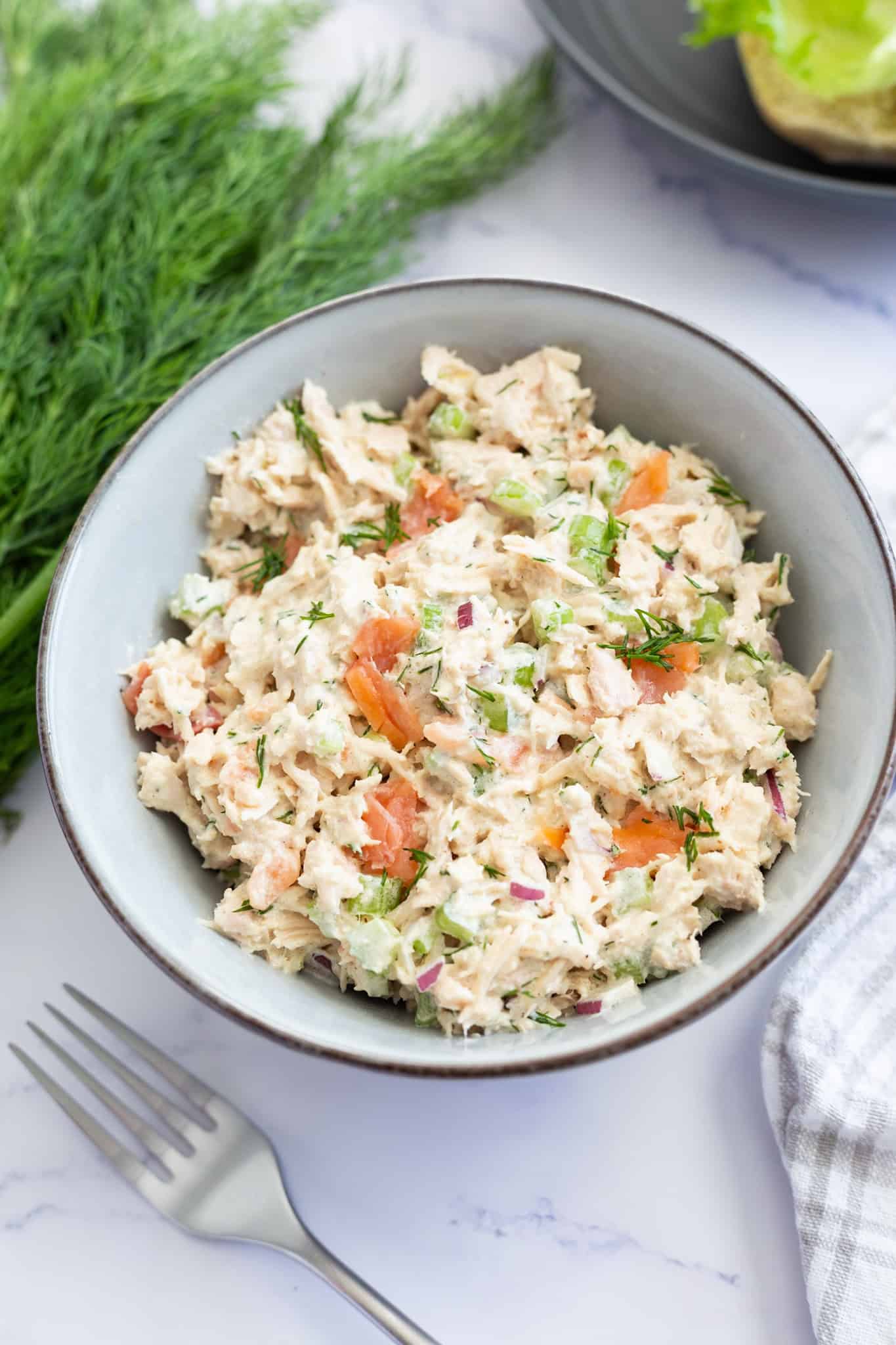 A bowl of tuna salad flecked with smoked salmon and garnished with fresh dill.