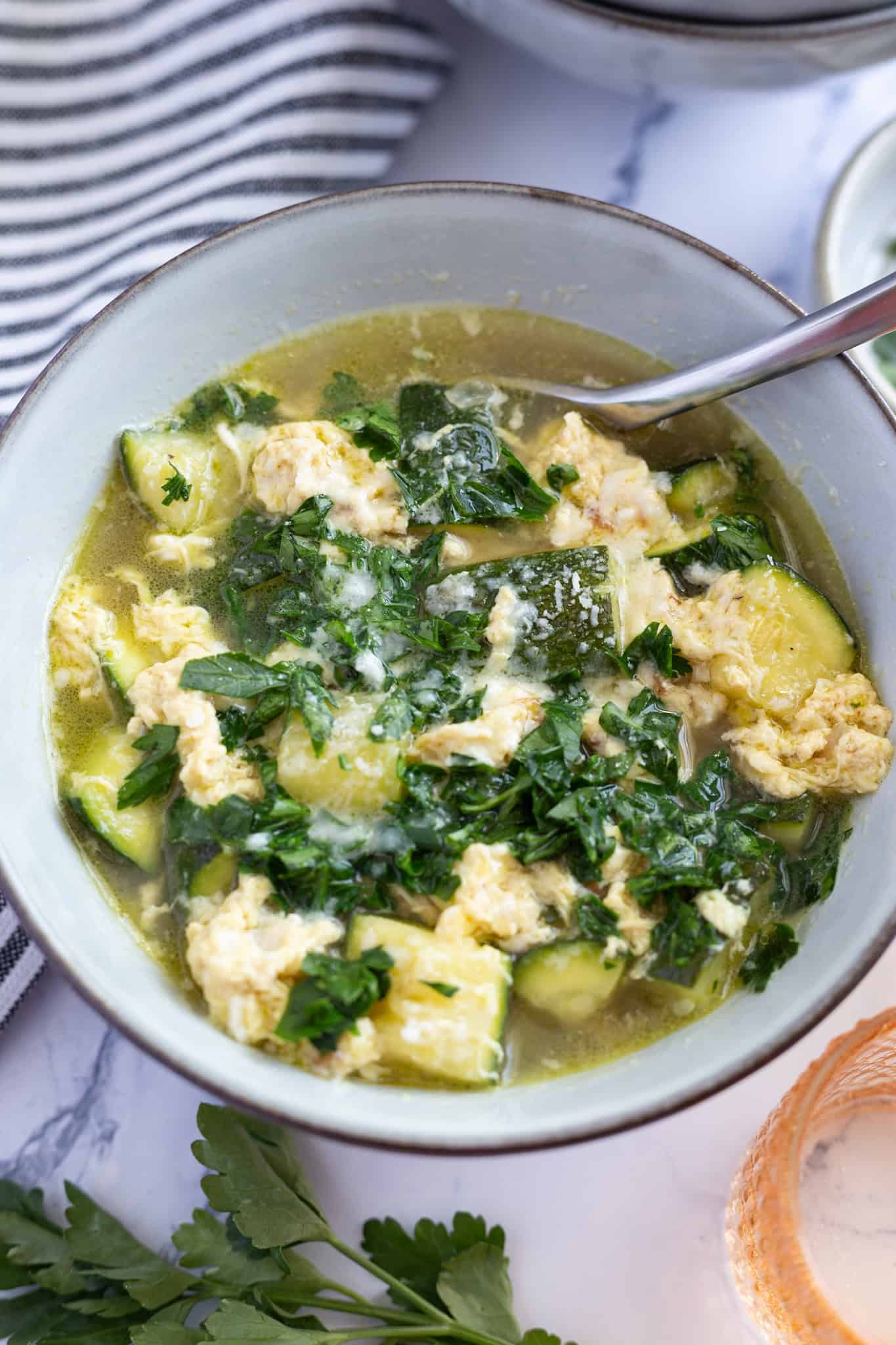 A bowl of Italian zucchini soup garnished with fresh minced parsley.