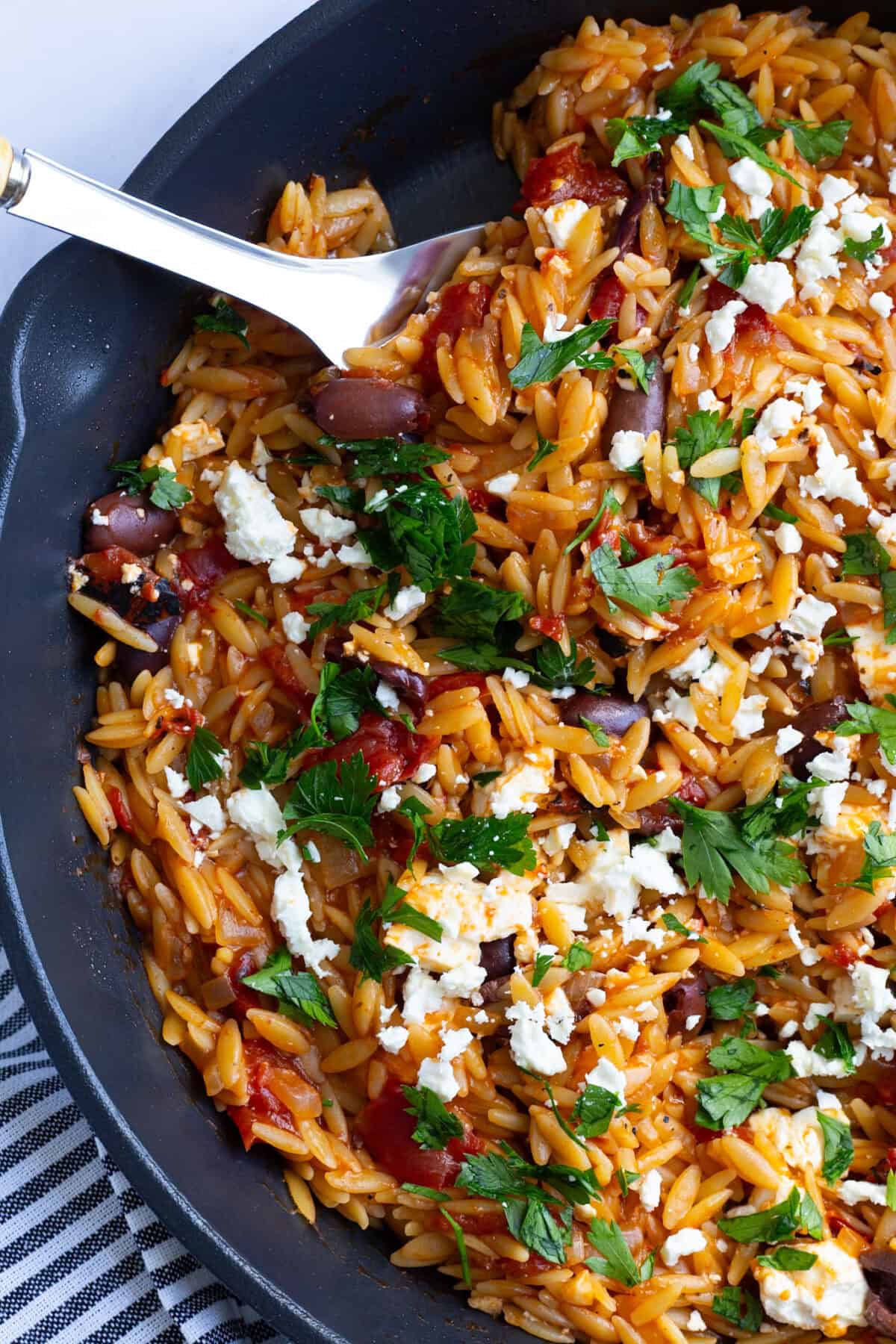 A pan of orzo with fire-roasted tomatoes, feta, and olives.