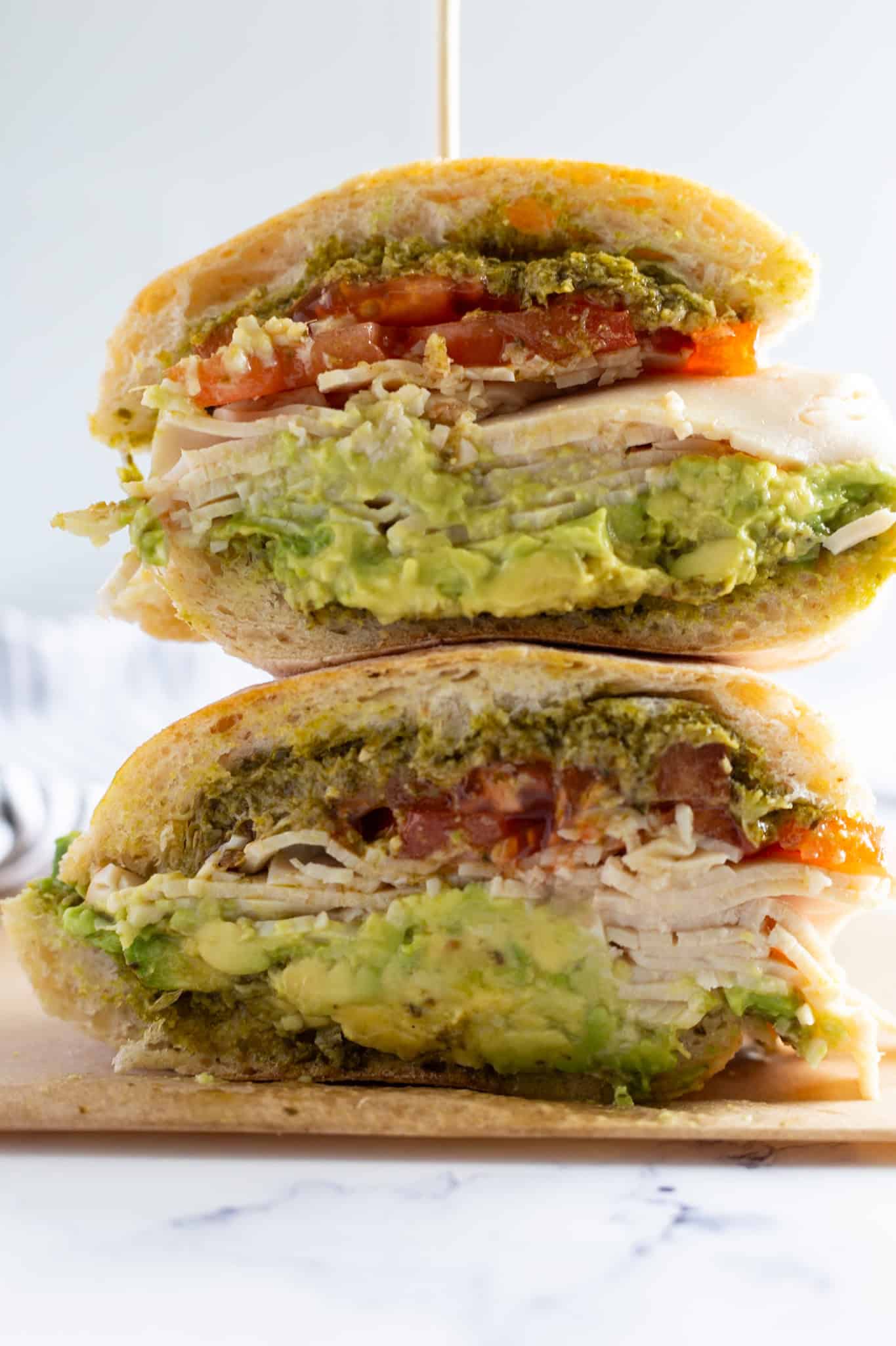 A stacked smoked turkey sandwich with avocado and pesto.