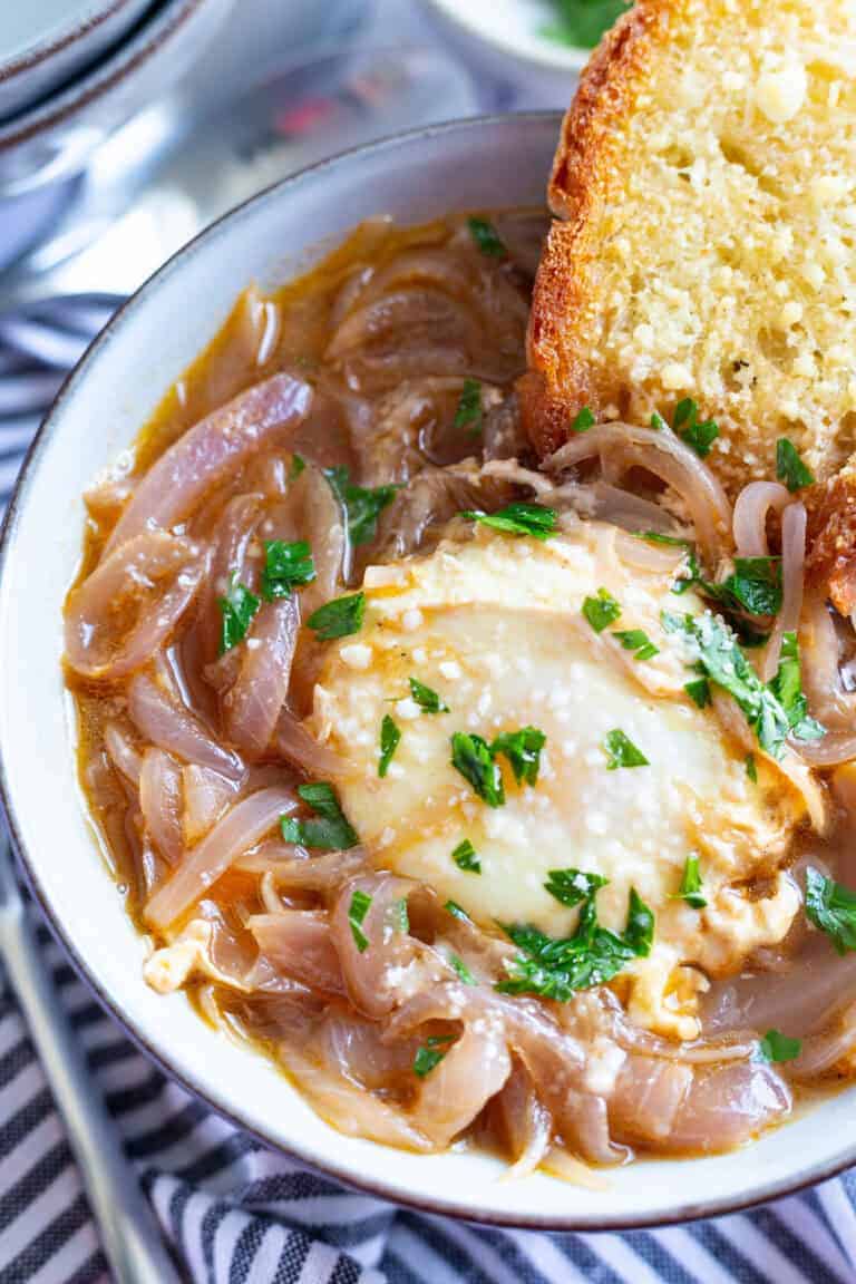 A bowl of Tuscan onion soup topped with a poached egg and with a slice of toasted cheesy bread.