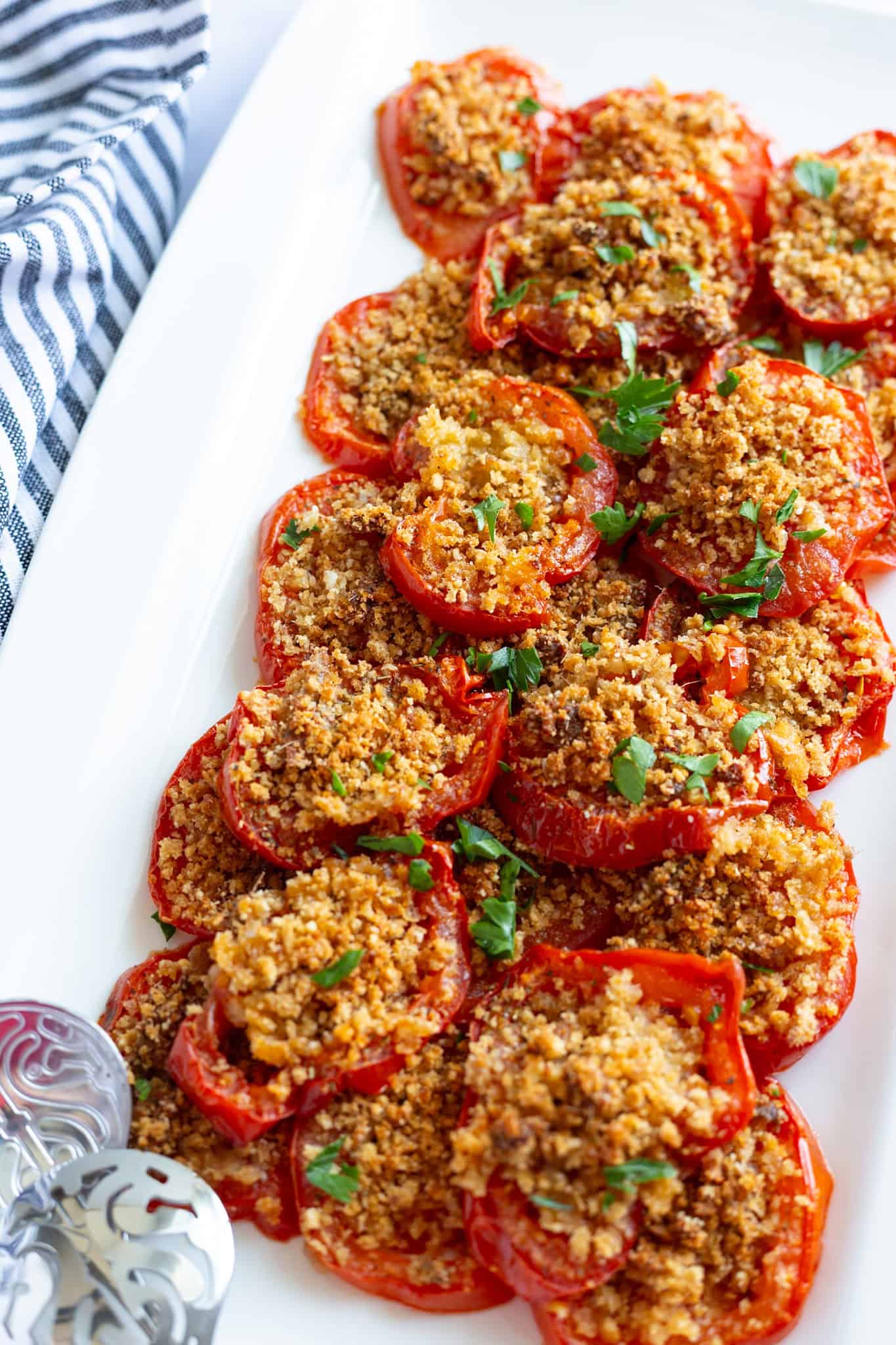 A white platter filled with roasted tomatoes topped with seasoned anchovy breadcrumbs.