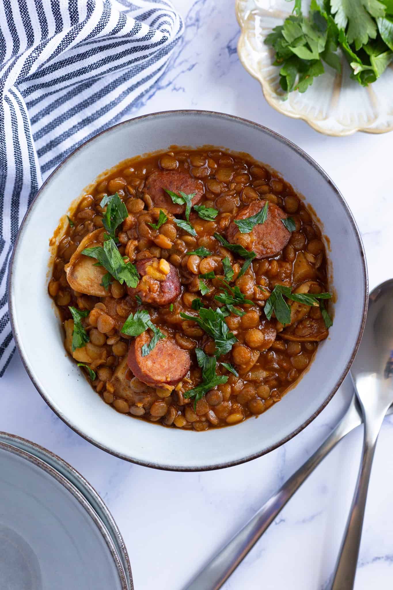 A bowl of lentil, chorizo, and potato stew garnished with fresh parsley.