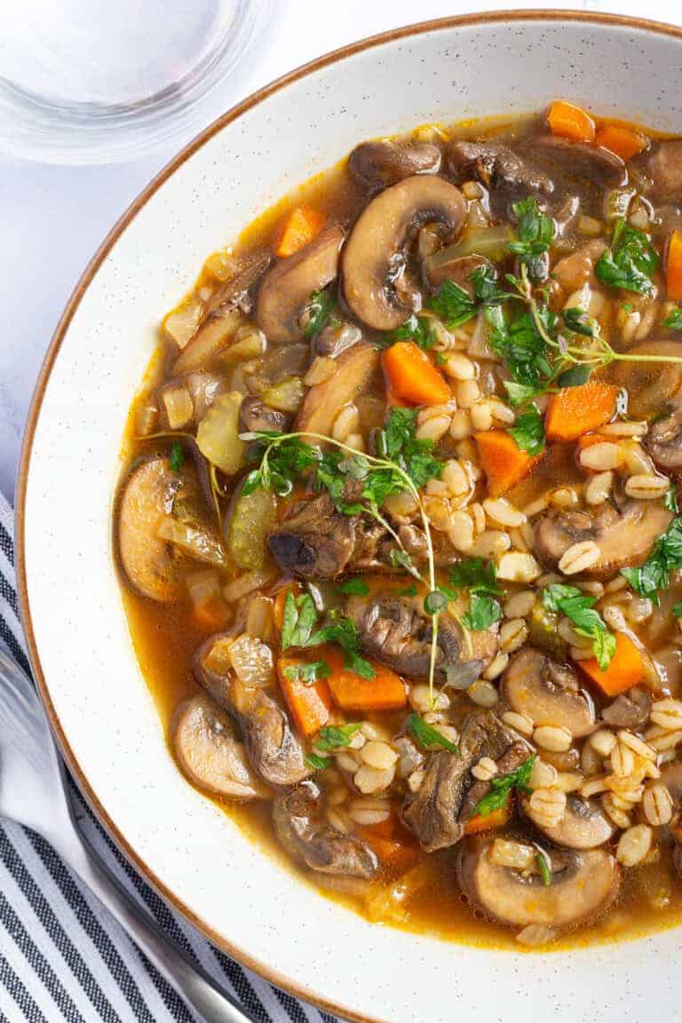 A bowl of mushroom and barley soup, garnished with thyme and parsley.