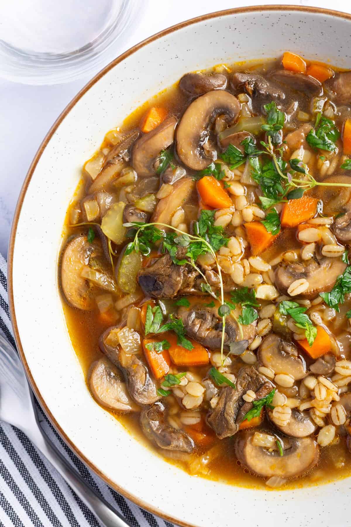 A bowl of mushroom and barley soup, garnished with thyme and parsley.