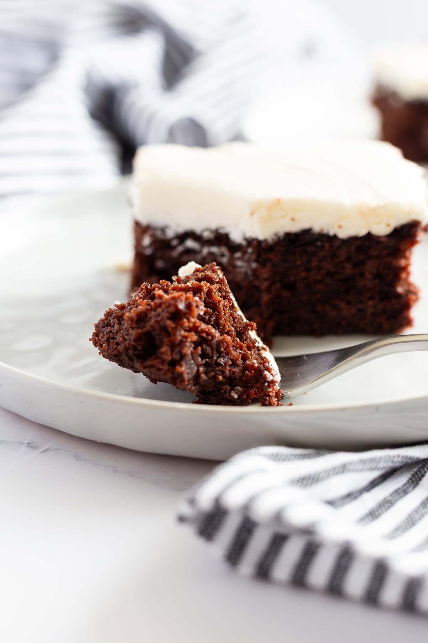 A slice of the best moist buttermilk chocolate cake with white frosting.