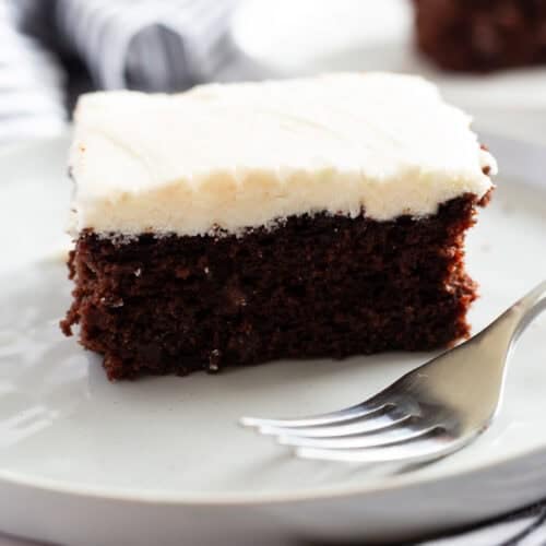 A slice of moist chocolate cake with white buttermilk frosting.