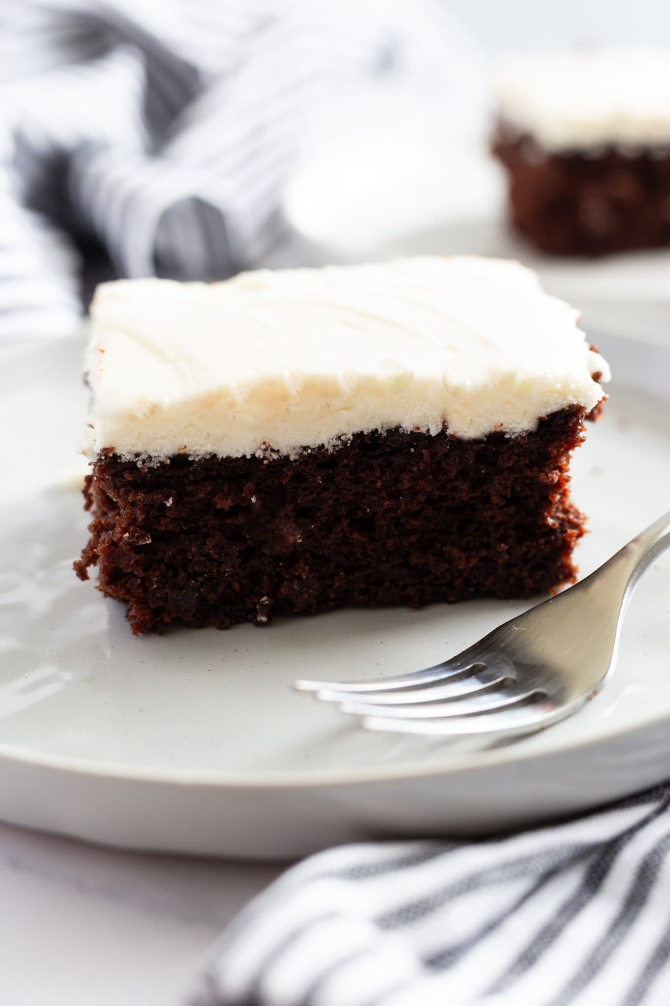 A slice of moist chocolate cake with white buttermilk frosting.