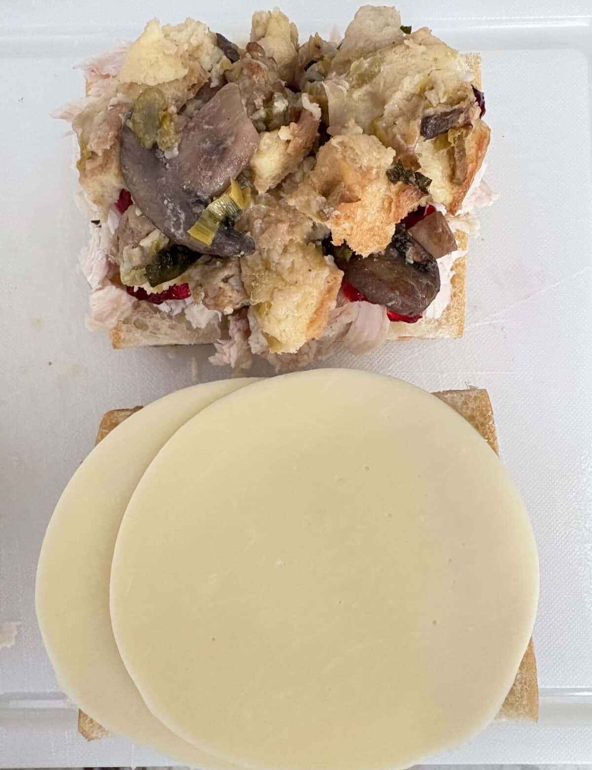 A slice of bread with turkey, cranberry sauce, and stuffing, and another slice with provolone.
