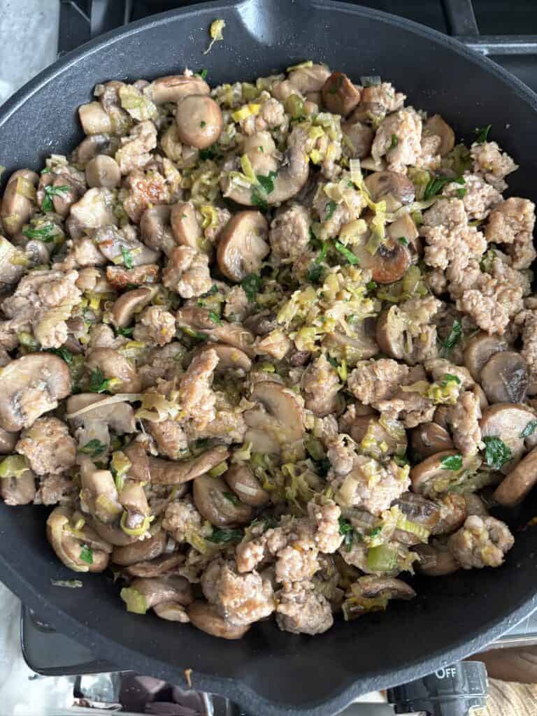 A pan of cooked mushrooms, leeks, and sausage.