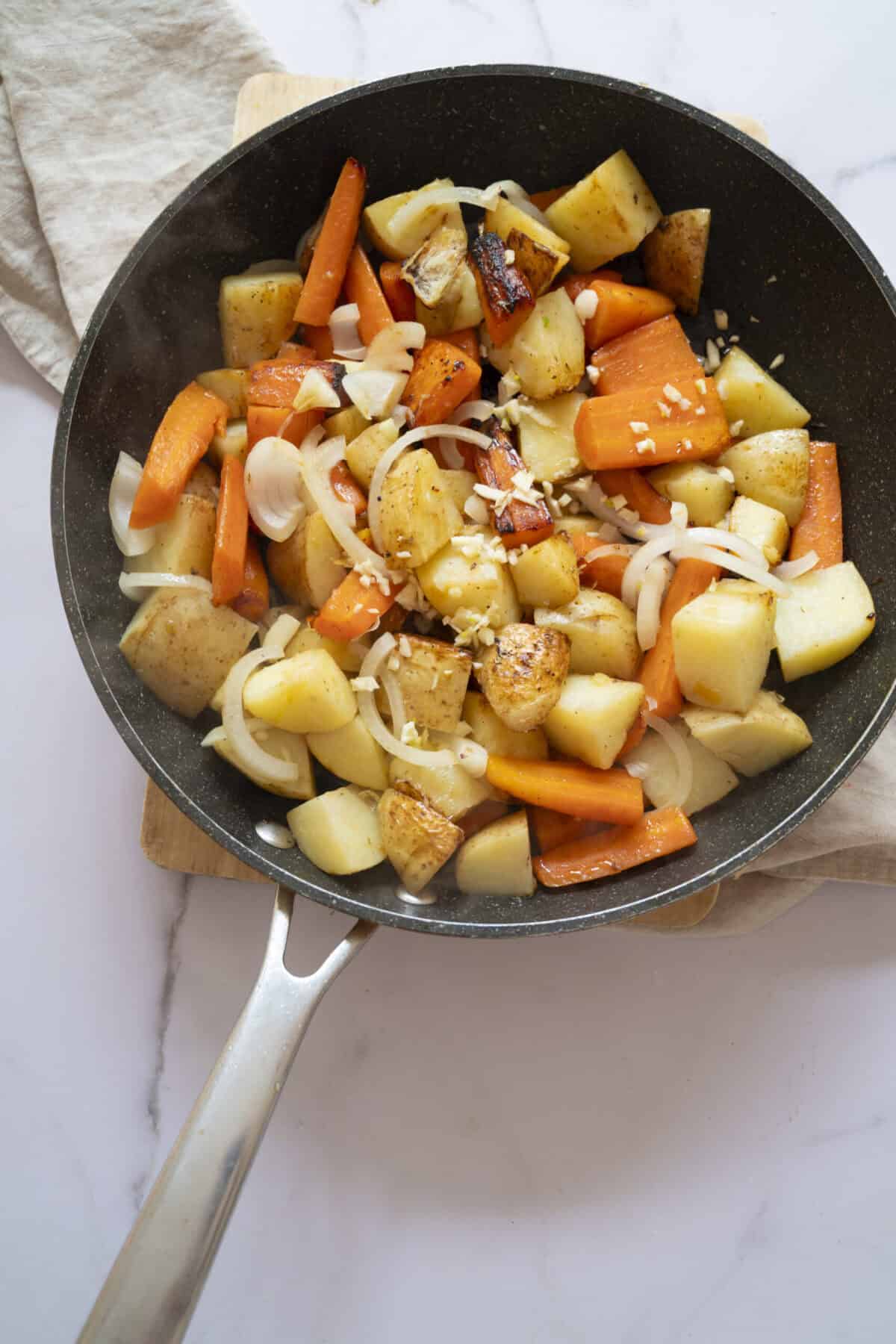 A pan of potatoes and carrots cooked with onions and garlic.