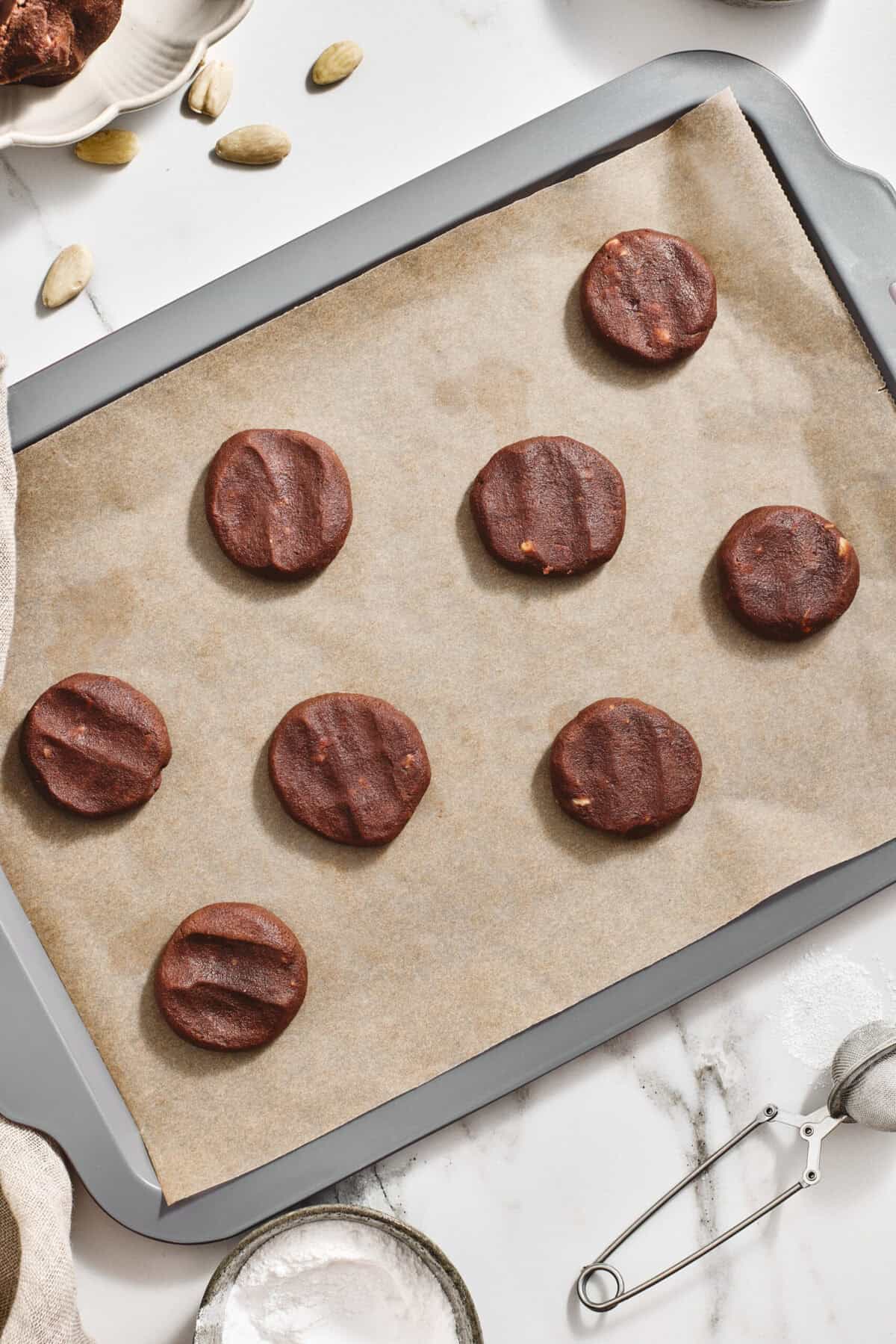 Flattened balls of raw cookie dough on a baking sheet.