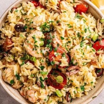 A bowl of orzo salad with shrimp, tomatoes, olives, and herbs.
