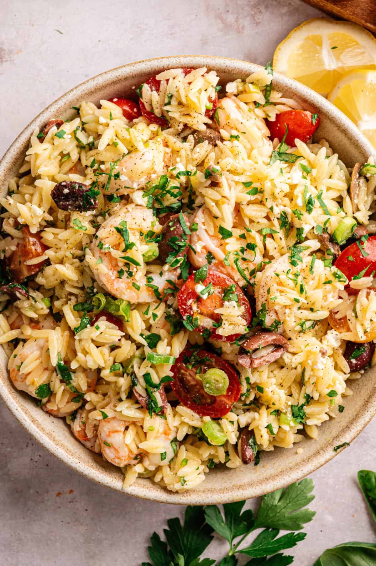 A bowl of orzo salad with shrimp, tomatoes, olives, and herbs.