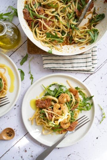 Plates of shrimp and chorizo pasta with arugula.