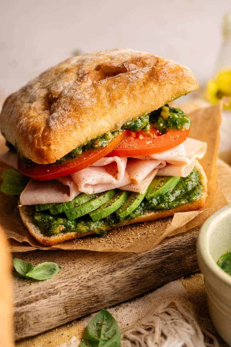 A smoked turkey sandwich with avocado and pesto.