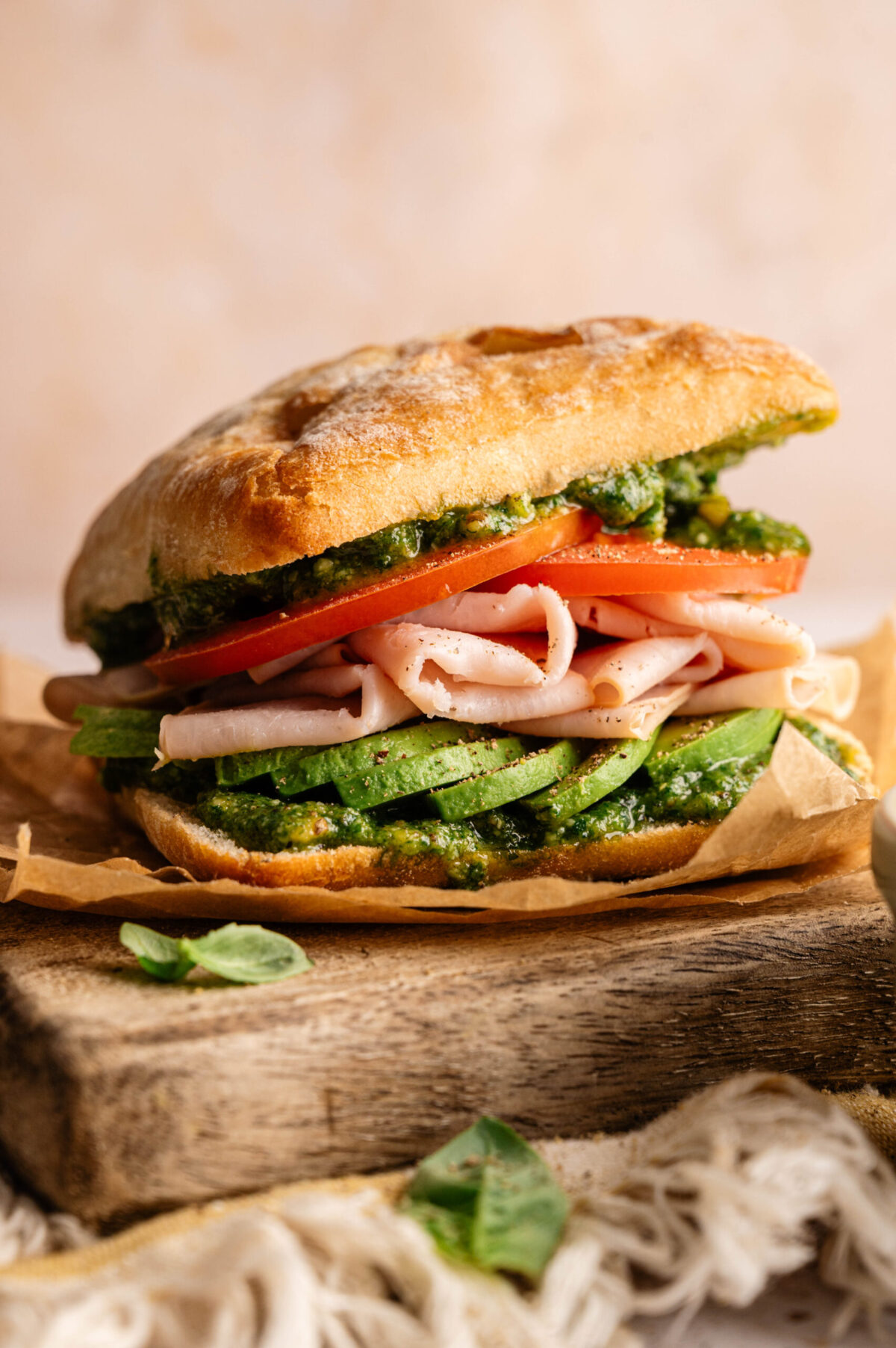 A smoked turkey sandwich with tomato, avocado, and pesto.