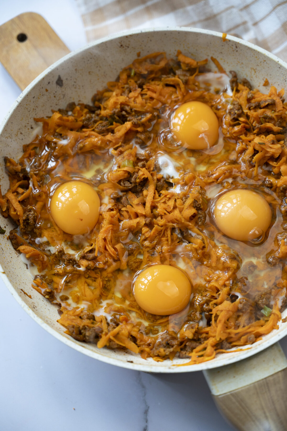 Four cracked eggs in a pan with shredded sweet potato and chorizo.