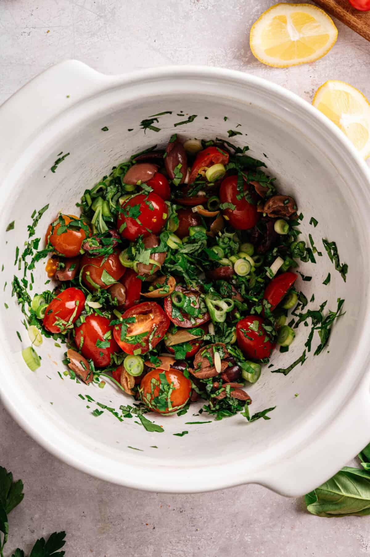 A bowl of cherry tomatoes, olives, and herbs.