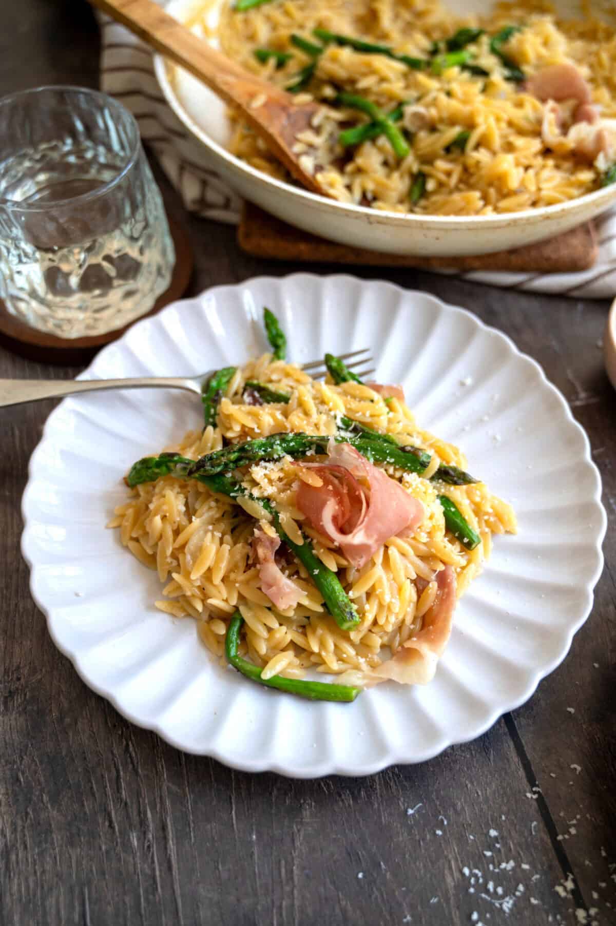 A plate of orzo with asparagus and torn prosciutto.