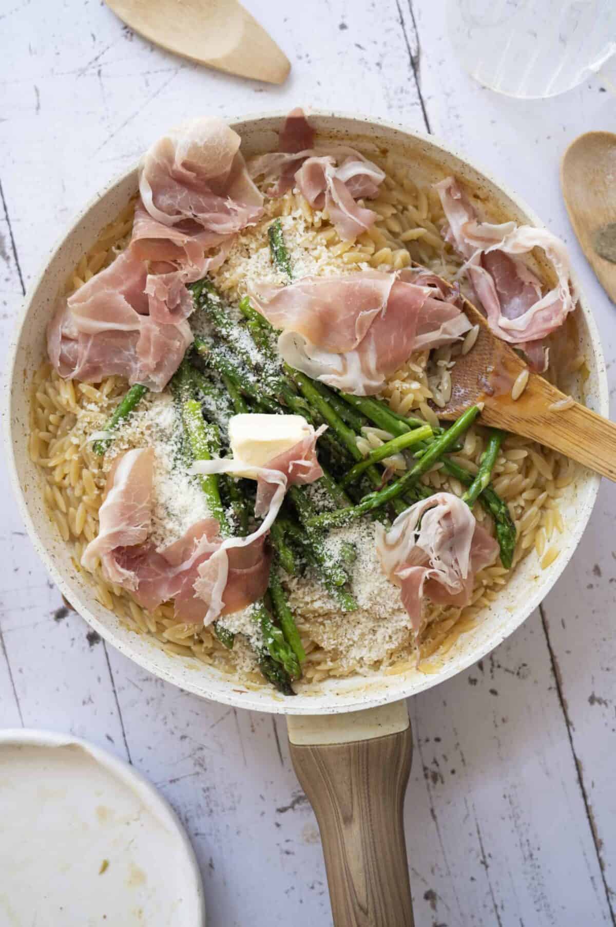 A pan of orzo tossed with asparagus and prosciutto.