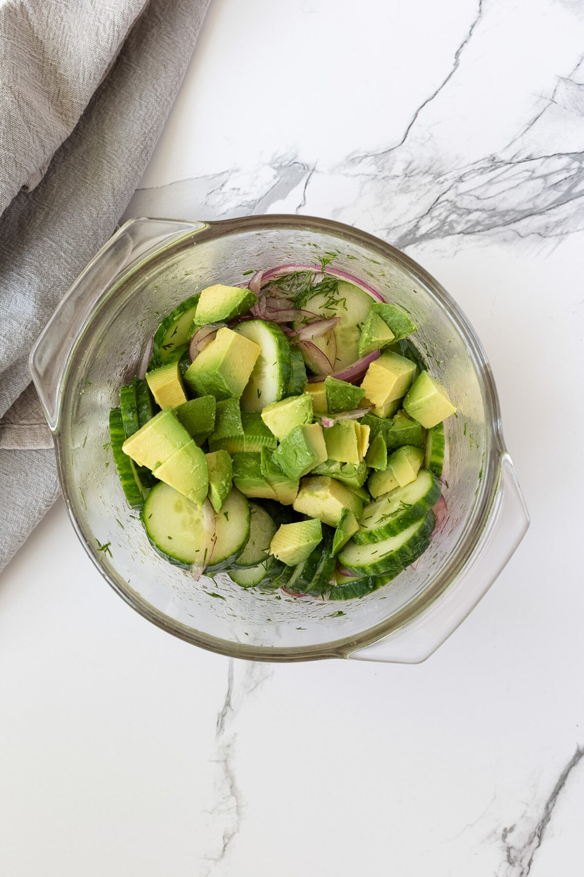 A bowl filled with sliced cucumbers, red onion, dill, and avocado.