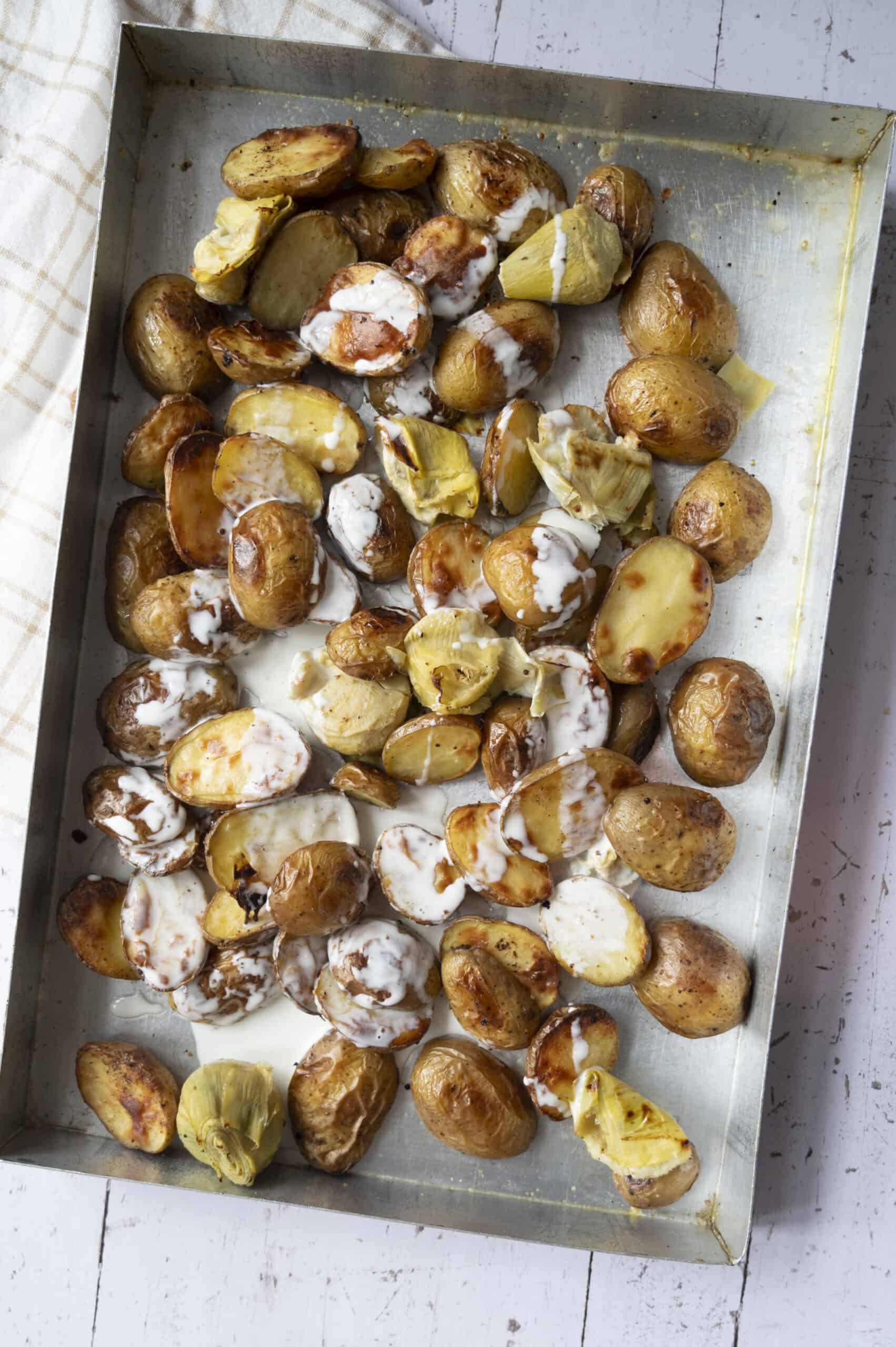 Potatoes and artichoke hearts in a pan with heavy cream added.