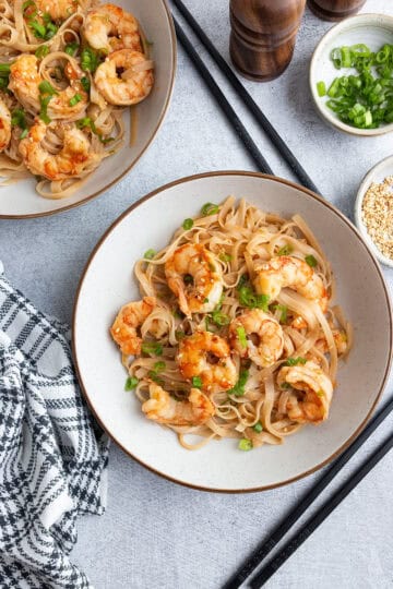 Garlic noodles with shrimp, topped with scallions and sesame seeds.