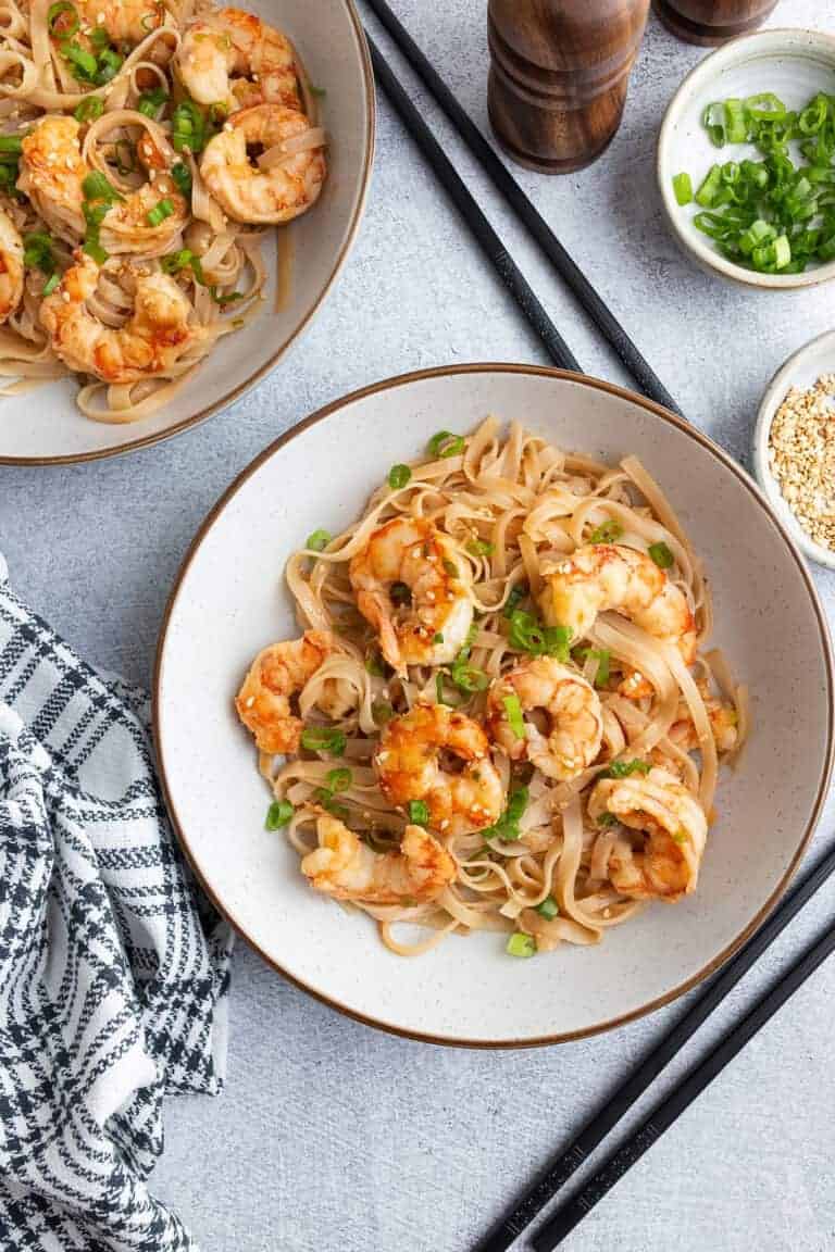 Garlic noodles with shrimp, topped with scallions and sesame seeds.