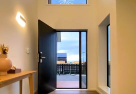 Modern NZ home entryway with black door and large glass windows, welcoming atmosphere.