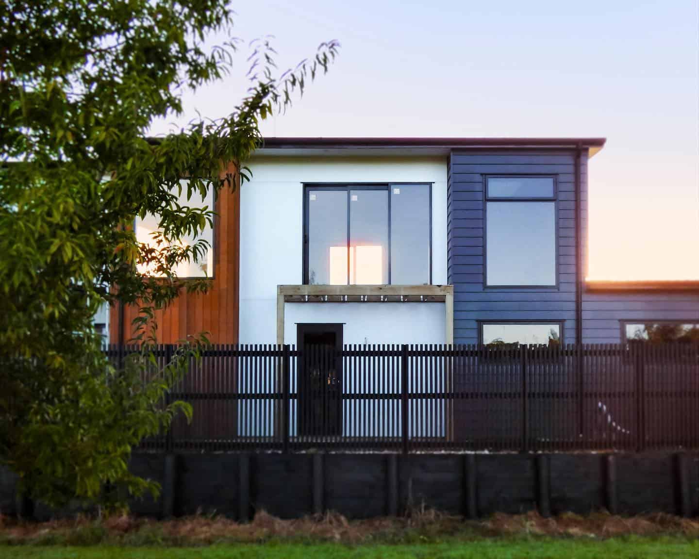 Contemporary modern house with colourful facade, large windows, and black fencing in a suburban neighbourhood.